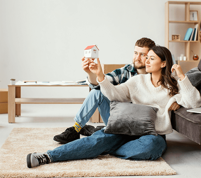 Couple sitting on floor and holding up a paper house.